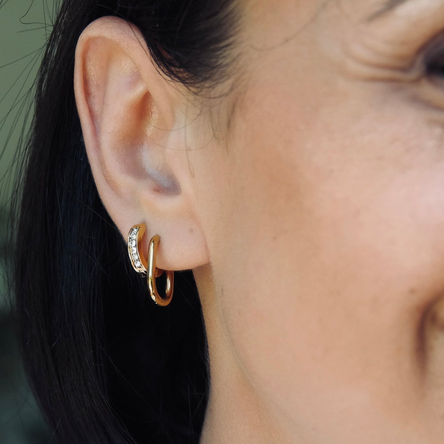 Close-up of a person wearing a gold hoop earring with a blurred background. Gold cubic zirconia huggie hoop water proof , gym proof jewellery