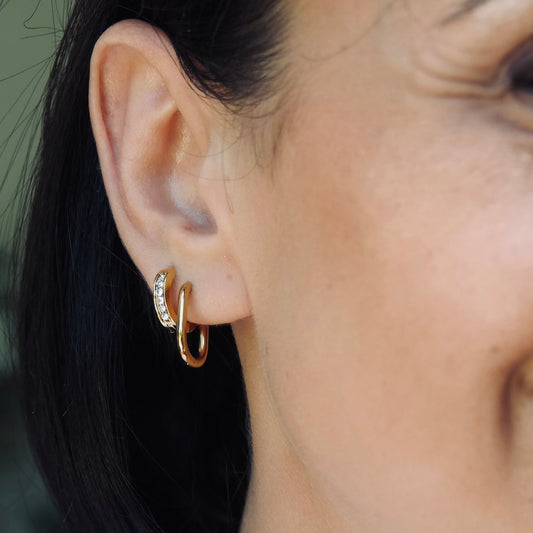 Close-up of a person wearing a gold hoop earring with a blurred background. Gold cubic zirconia huggie hoop water proof , gym proof jewellery
